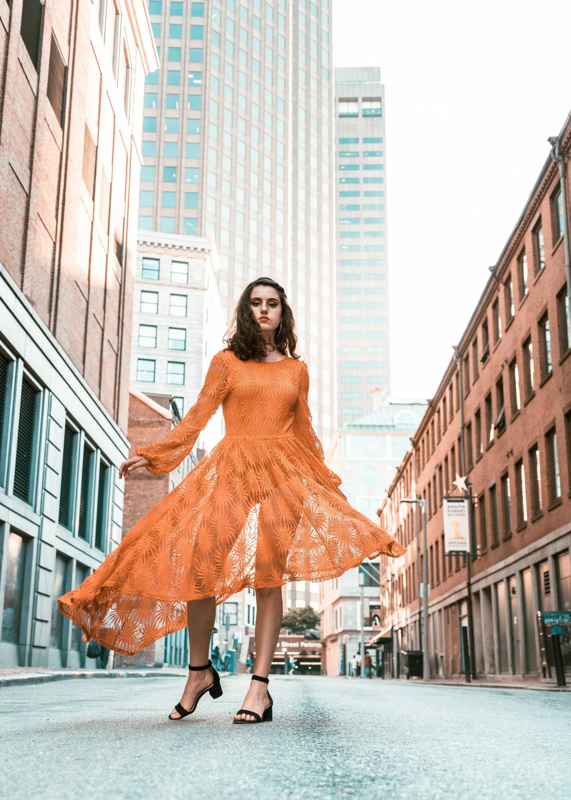 woman in orange long-sleeved dress between buildings during daytime